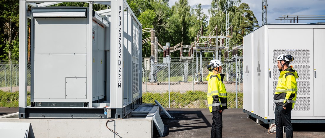 Två personer i varselkläder står bredvid ett av Ingrid Capacitys batterier.