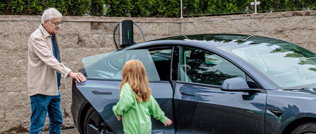 Äldre man och barn bredvid en elbil och solceller på ett hustak