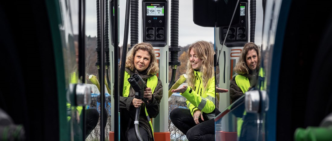 Två kvinnor i färd med att sätta i en laddhandske i en elbuss.