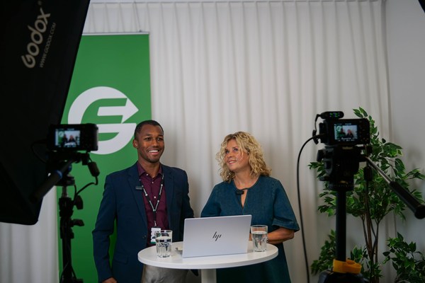 En välklädd man och kvinna står i en filmstudio och förbereder sig inför sändning av webinar.