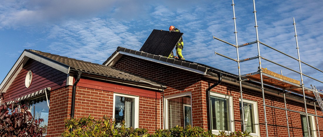 En solcellsmontör lägger en solpanel på ett villatak.