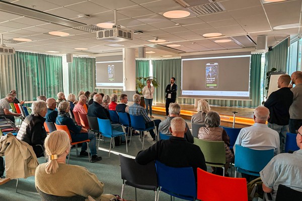 En sal med pensionärer som lyssnar på en utbildning om hur man använder Göteborg Energi-appen. Längst fram i salen står en man och en kvinna och håller i föreläsningen stående framför en skärm som visar hur appen fungerar.