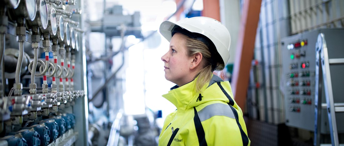 En av Göteborg Energis medarbetare står i en hall och jobbar, iklädd varselkläder och med skyddshjälm på huvudet.