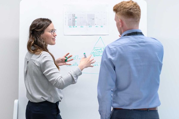 En kvinna står framför en whiteboardtavla och diskuterar med en man