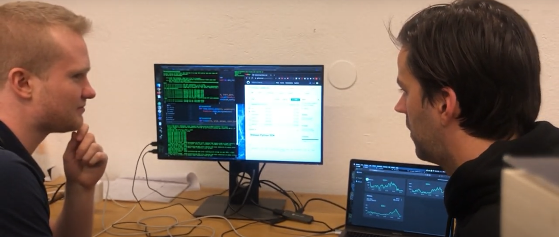 Två män sitter framför en datorskärm fylld med kod.
