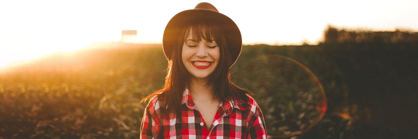 En ung kvinna i rutig skjorta står mitt i ett fält med ett stort leende på läpparna.