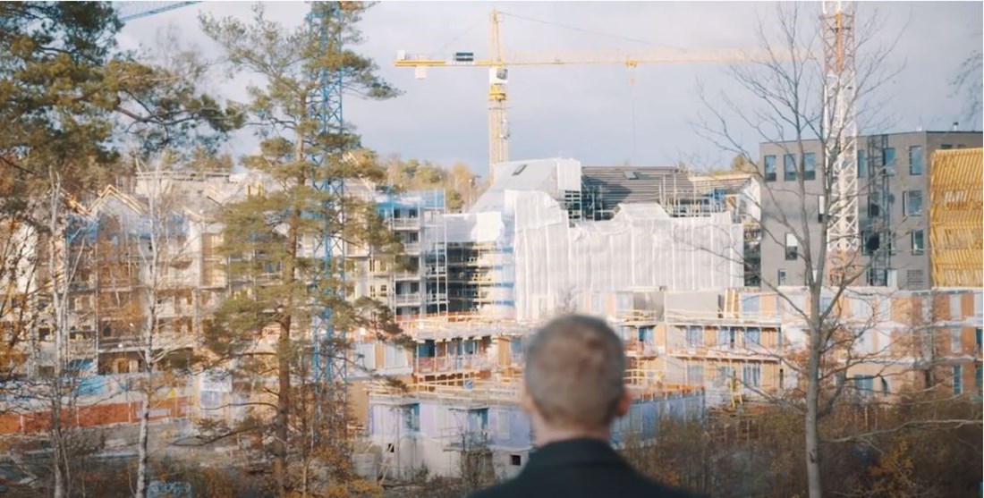 I förgrunden en man som står med ryggen mot kameran och beskådar ett stort byggarbete.