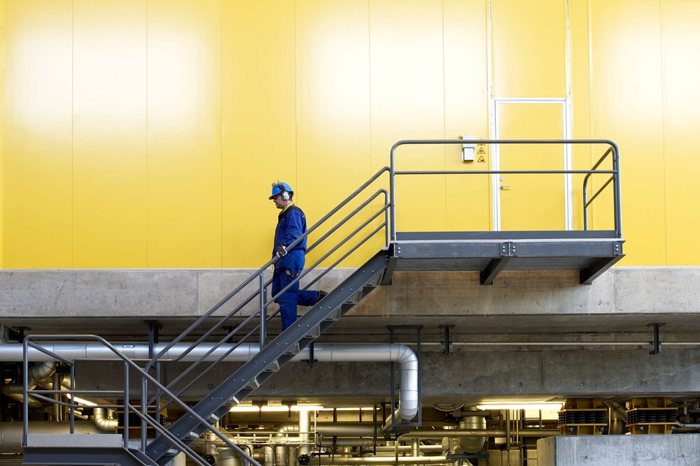 Interiör Rya kraftvärmeverk - en anställd går ner för en trappa med en gul vägg som bakgrund.