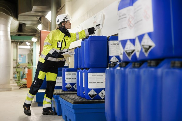 En medarbetare på Göteborg Energi kontrollerar ett dokument som hänger ovanför ett par blåa tunnor.